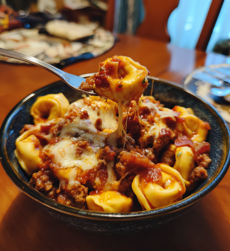 Hearty meat lovers tortellini pasta with savory meat sauce and a melted cheese pull.