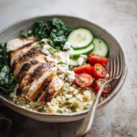 Grilled chicken quinoa bowl with spinach, cucumber, cherry tomatoes, and crumbled feta cheese.