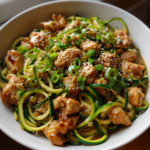 Garlic chicken zucchini noodles stir fry with sesame seeds and sliced green onions.